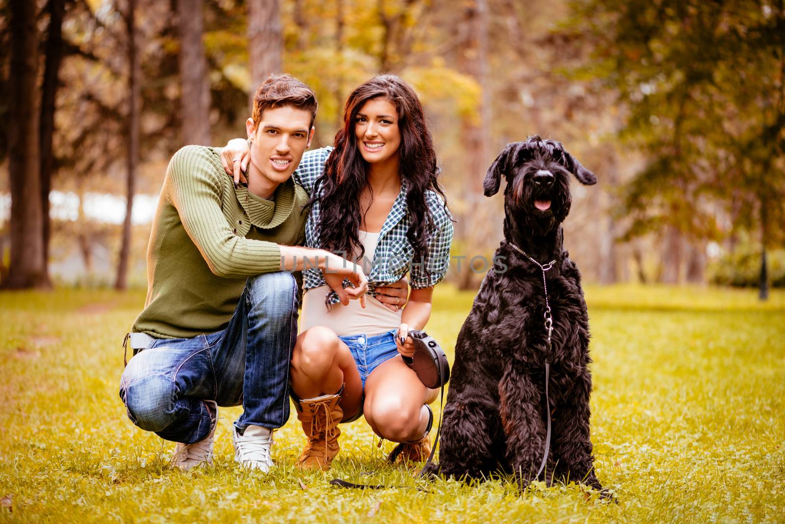 Beautiful lovely couple with a black giant schnauzer enjoying in the park. Looking at camera.