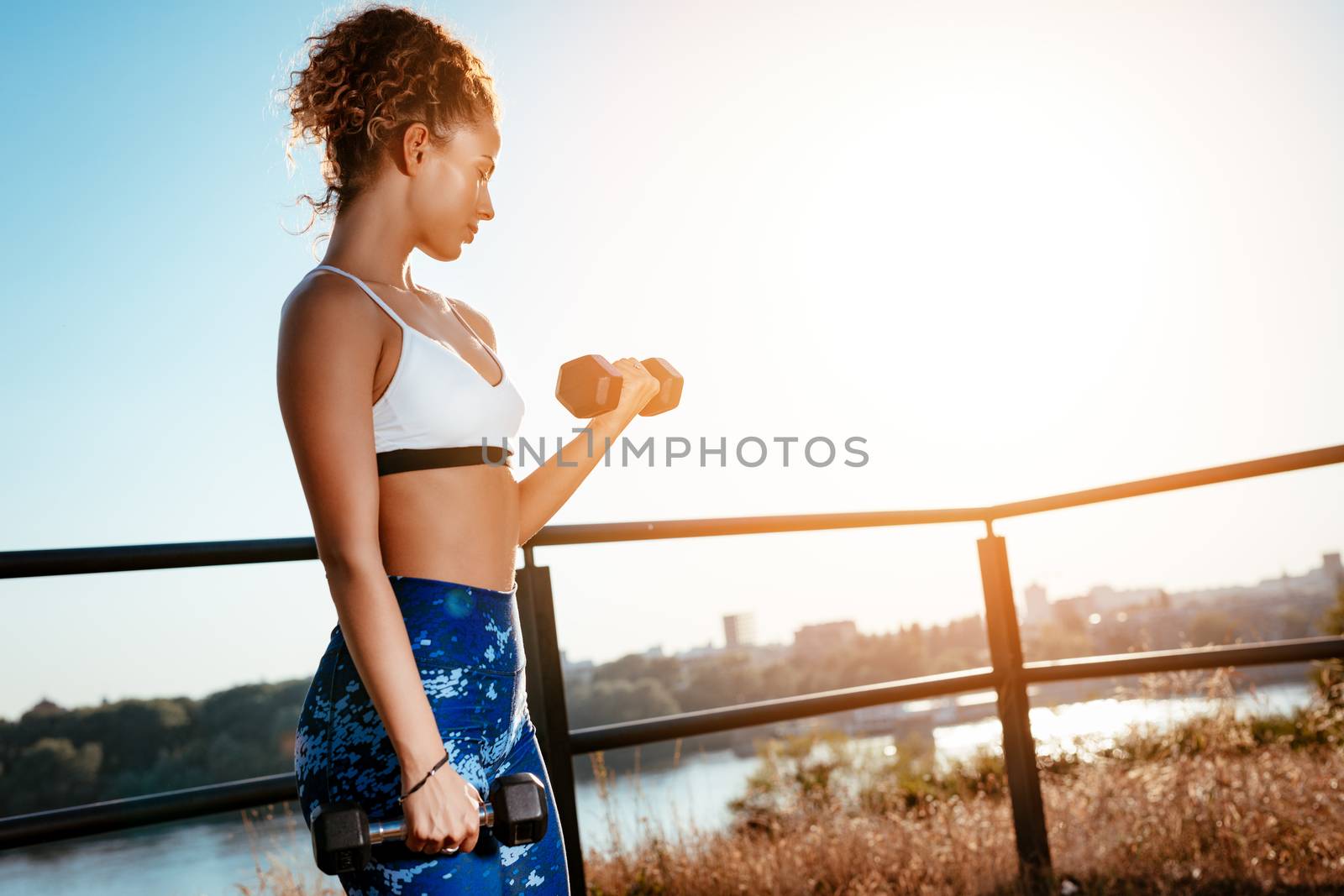 Young fitness woman doing exercise with dumbbell on the city rooftop.