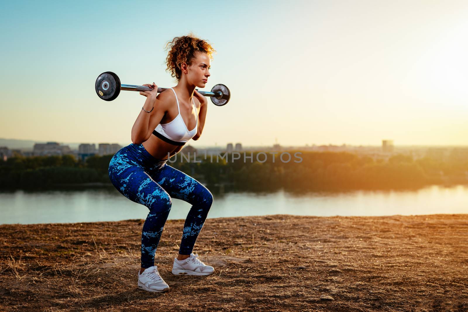 Young fitness woman doing workout with dumbbell by river on the city rooftop.