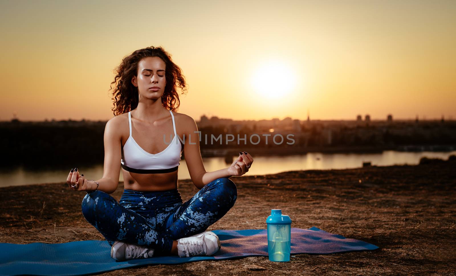 Young fitness woman doing yoga exercise on the city rooftop at sunset.