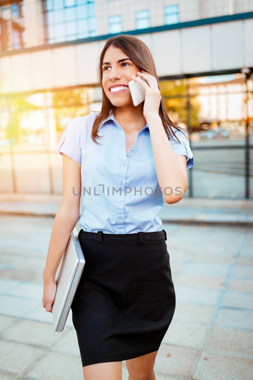 Young smiling businesswoman talking on smartphone in office district.