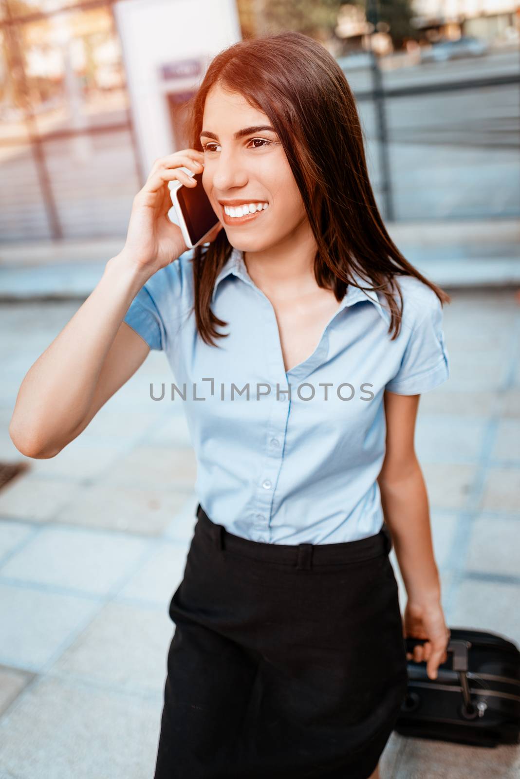 Young beautiful business woman walking with suitcase ready for a business trip and talking on mobile phone.