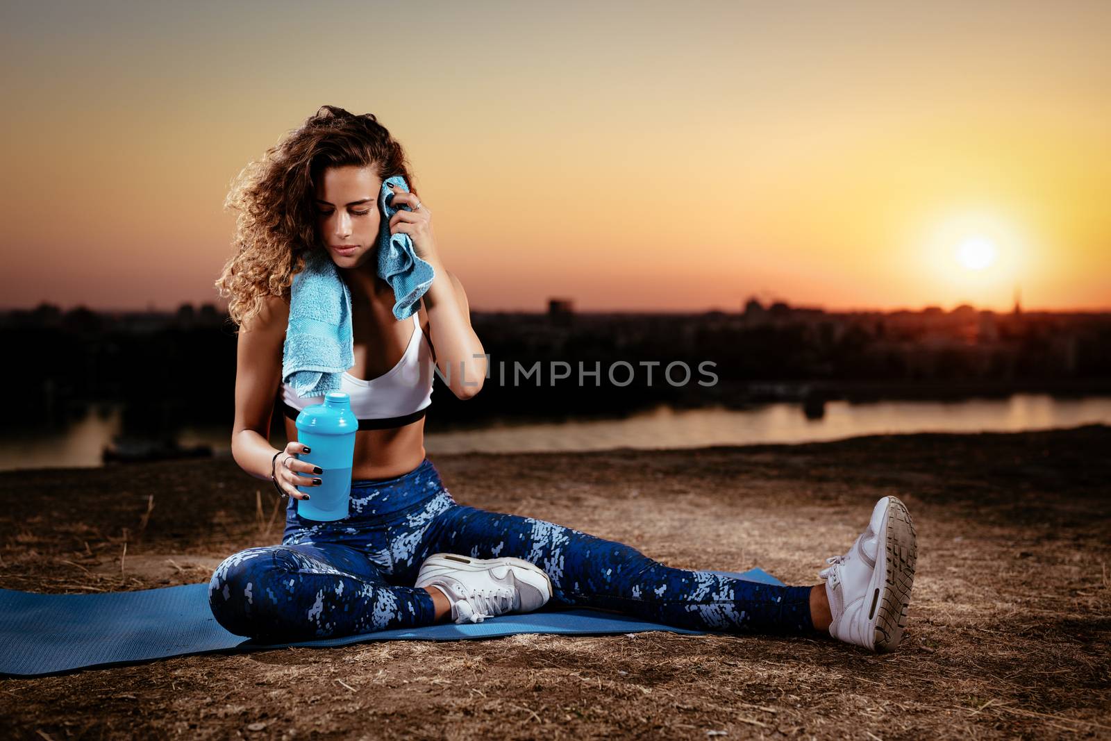 Young fitness woman resting afther hard training on the city rooftop at sunset.