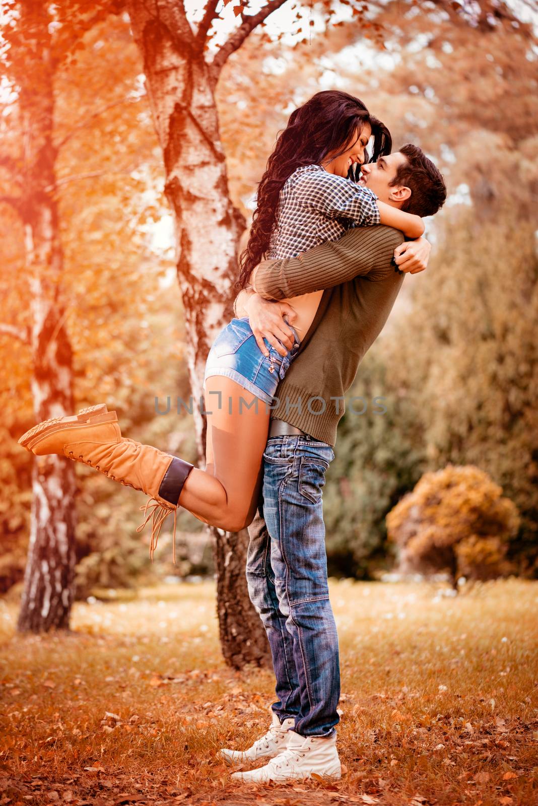 Beautiful lovely couple enjoying in sunny park in autumn colors. Guy holding girlfriend in height in a passionate embrace.