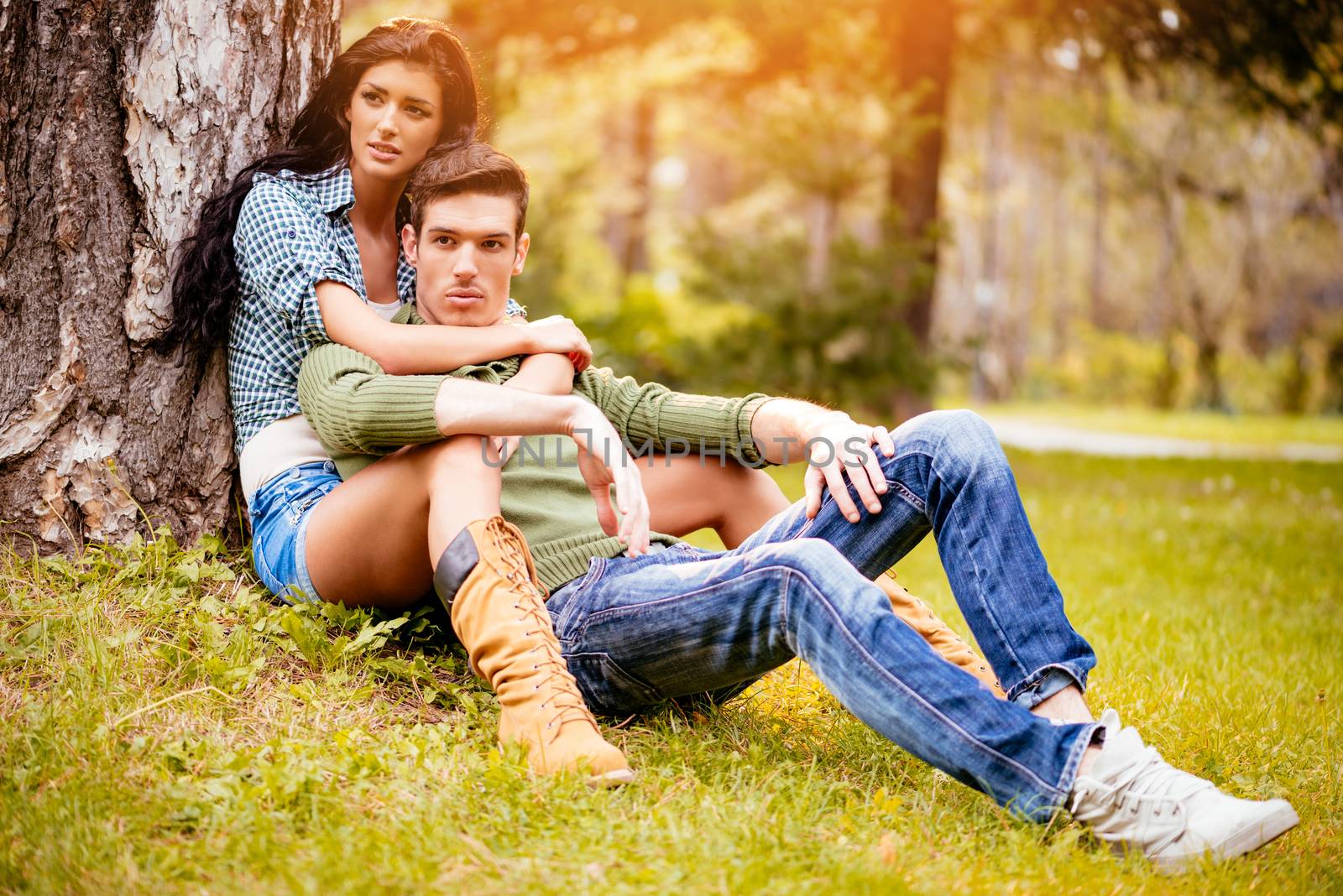 Beautiful lovely couple sitting on the grass next to the tree and enjoying in sunny park in autumn colors. 