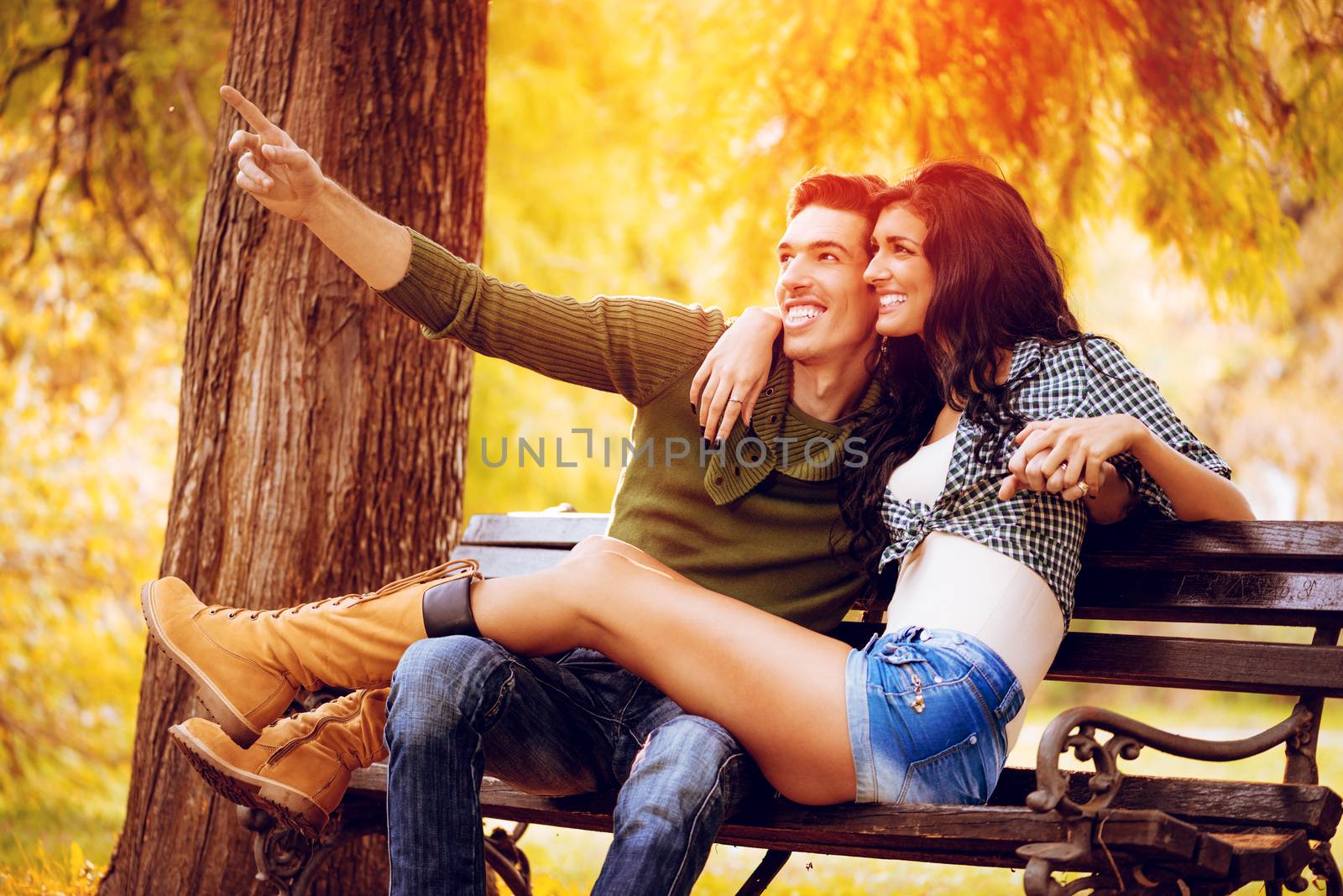 Beautiful lovely couple sitting on the bench and enjoying in sunny park in autumn colors.