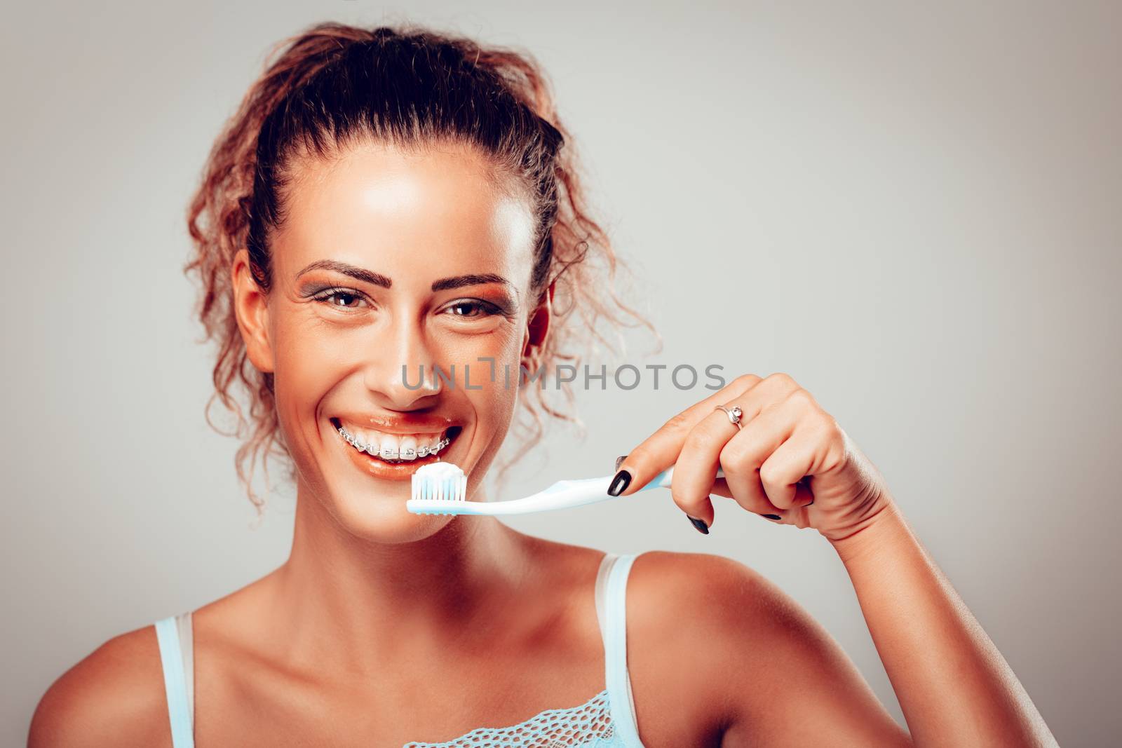 Smiling young woman with toothbrus showing her perfect white teeth with braces. Looking at camera.