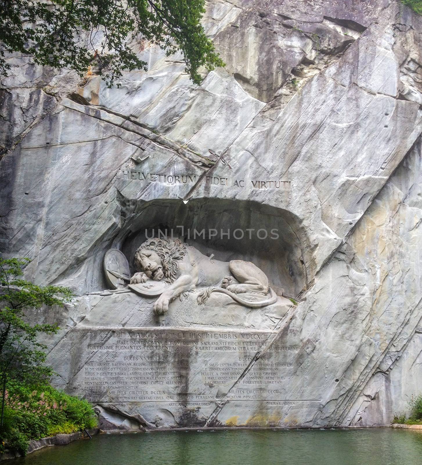 Dying lion monument (German: Lowendenkmal) carved on the face of stone cliff with the pond in the foreground in Luzern, Switzerland, Europe.