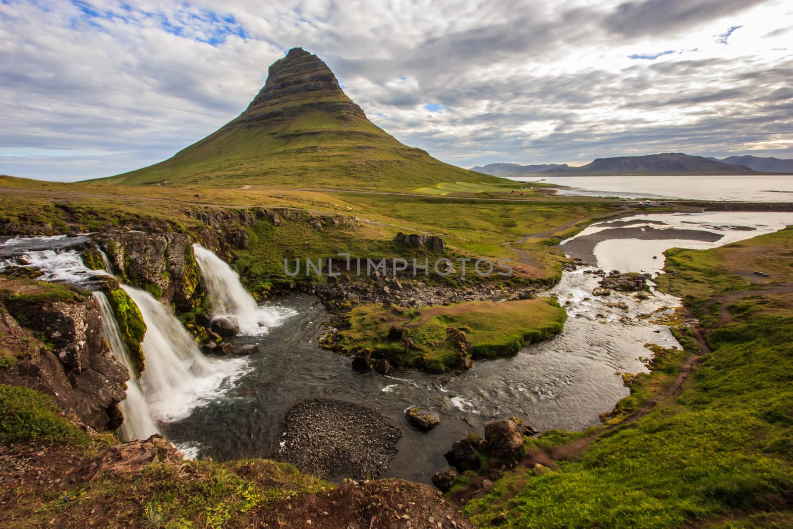 Summer cloudy day with Kirkjufell volcano on the coast of Snaefellsnes peninsula. Idyllic scene of Kirkjufellsfoss waterfall, Iceland, by victorflowerfly