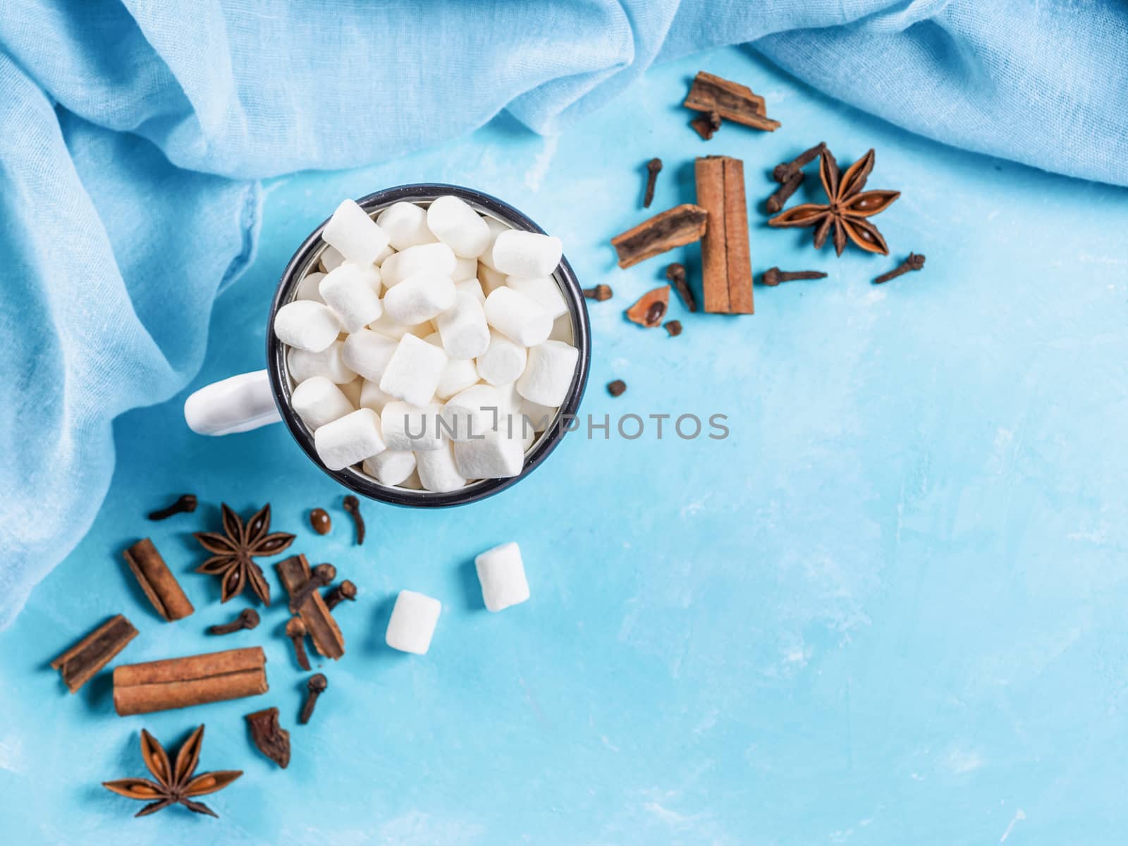 Marshmallows and winter spices on blue background with copyspace. Flat lay or top view. Background of colorful mini marshmallows, cinnamon, cloves and star anise. Winter food background concept.