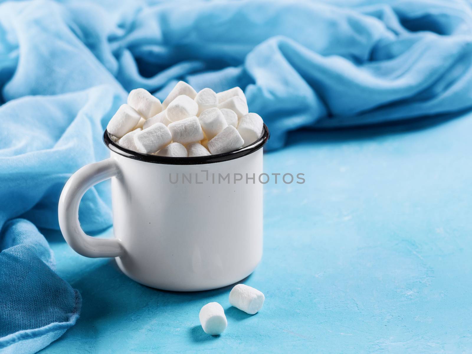 Marshmallows in cup on blue background with copyspace. Winter food background concept.