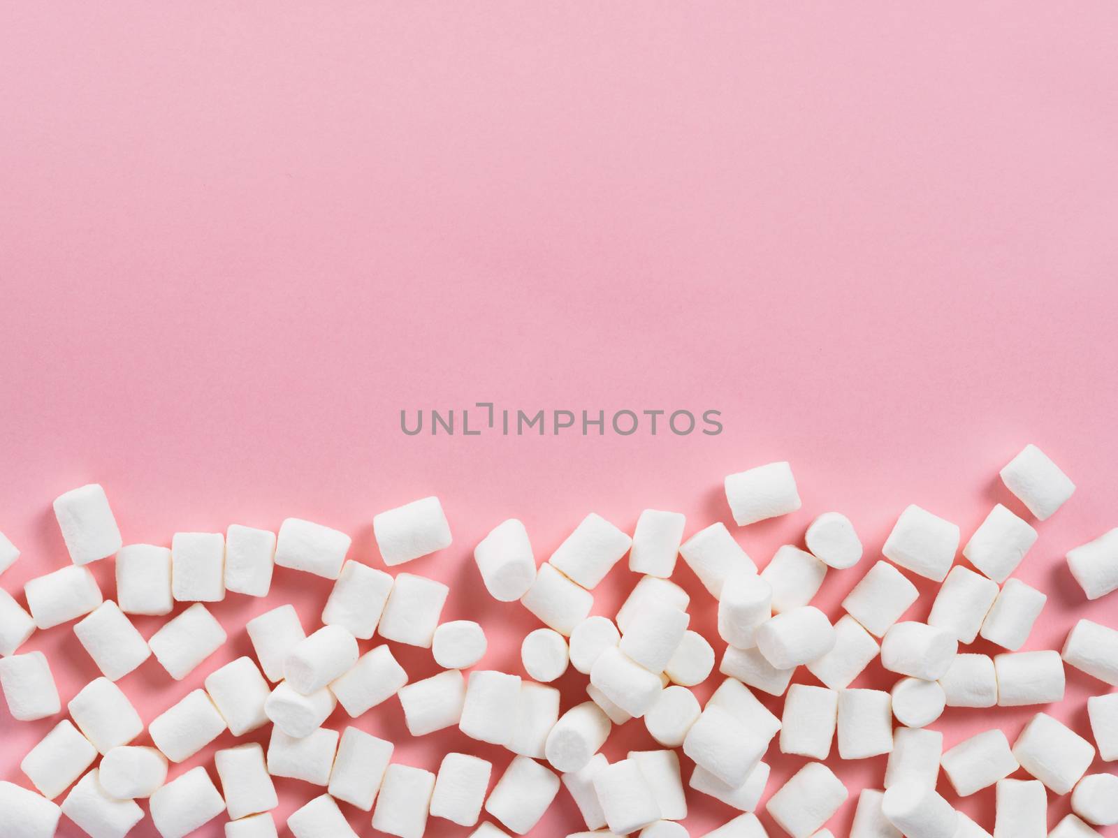 Marshmallows on pink background with copyspace. Flat lay or top view. Background or texture of colorful mini marshmallows. Winter food background concept.