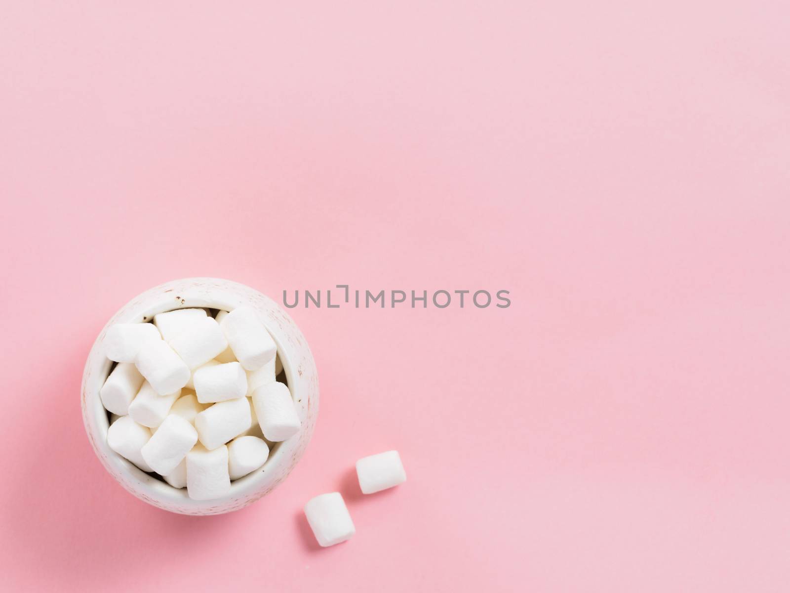 Marshmallows on pink background with copyspace. Flat lay or top view. Background or texture of colorful mini marshmallows. Winter food background concept.