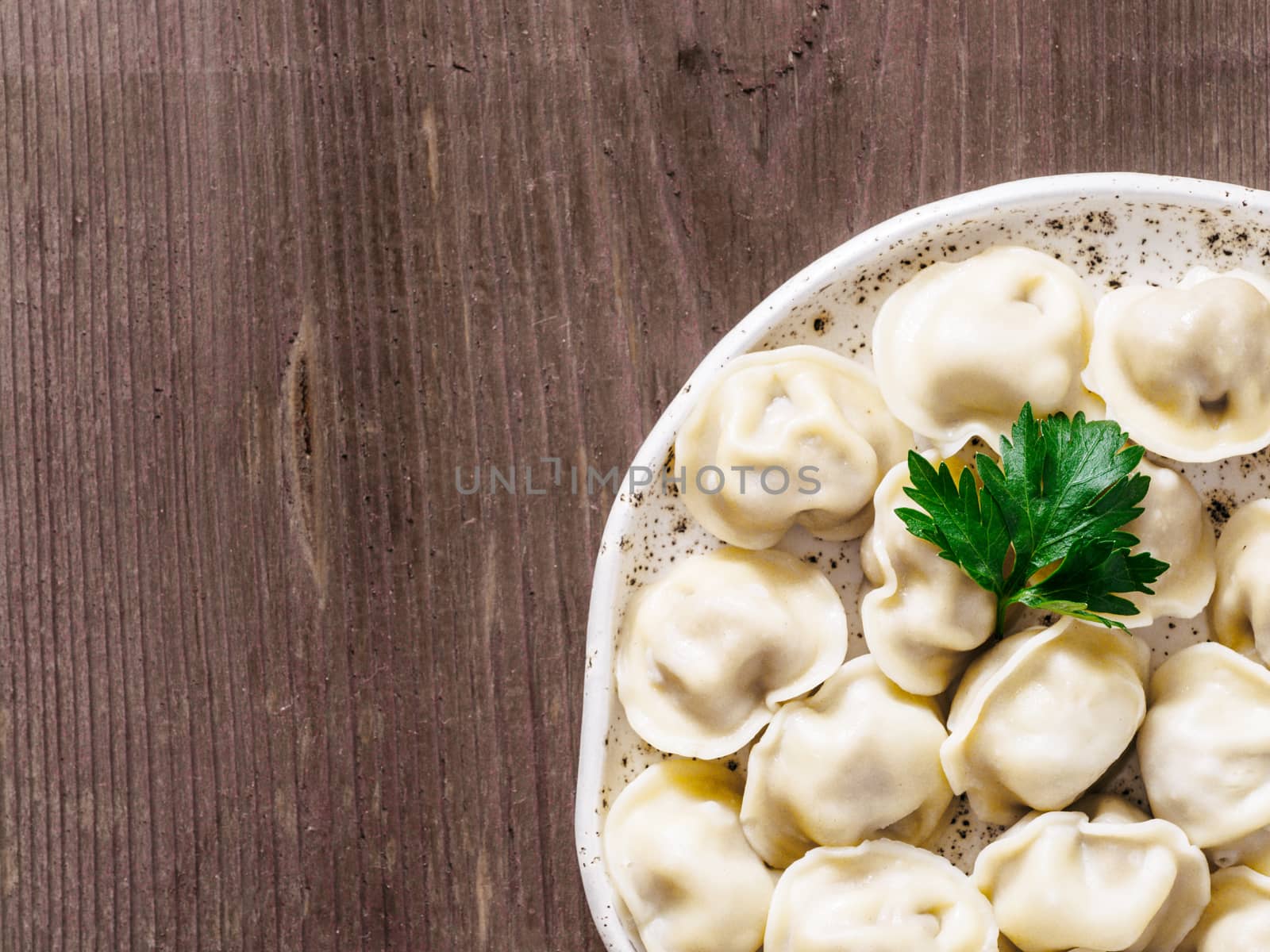 Close up viw of traditional russian pelmeni, ravioli, dumplings with meat on brown wooden background. Copyspace. Top view or flat lay. Russian food and russian kitchen concept.
