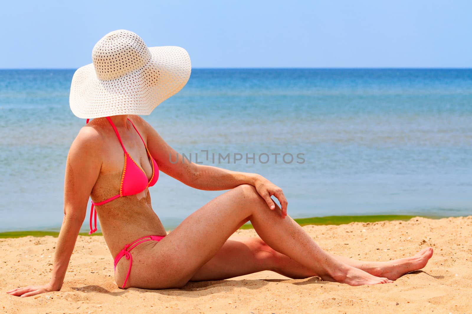 Woman in big straw sunhat sunbathing on a sandy beach. Summer holidays concept