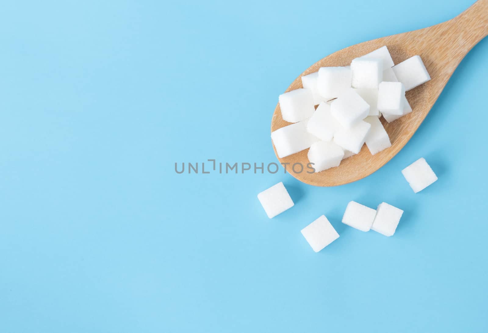 Closeup top view sugar cubes on wooden spoon white blue backgrou by pt.pongsak@gmail.com