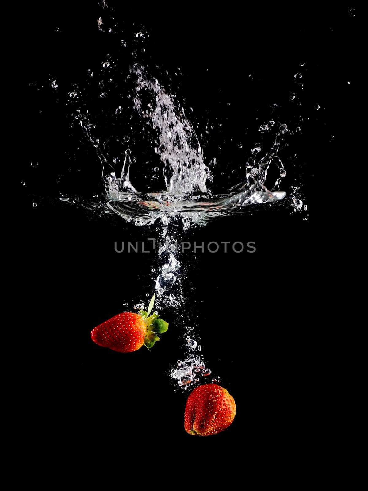 Fresh strawberry fruit making splash in water.