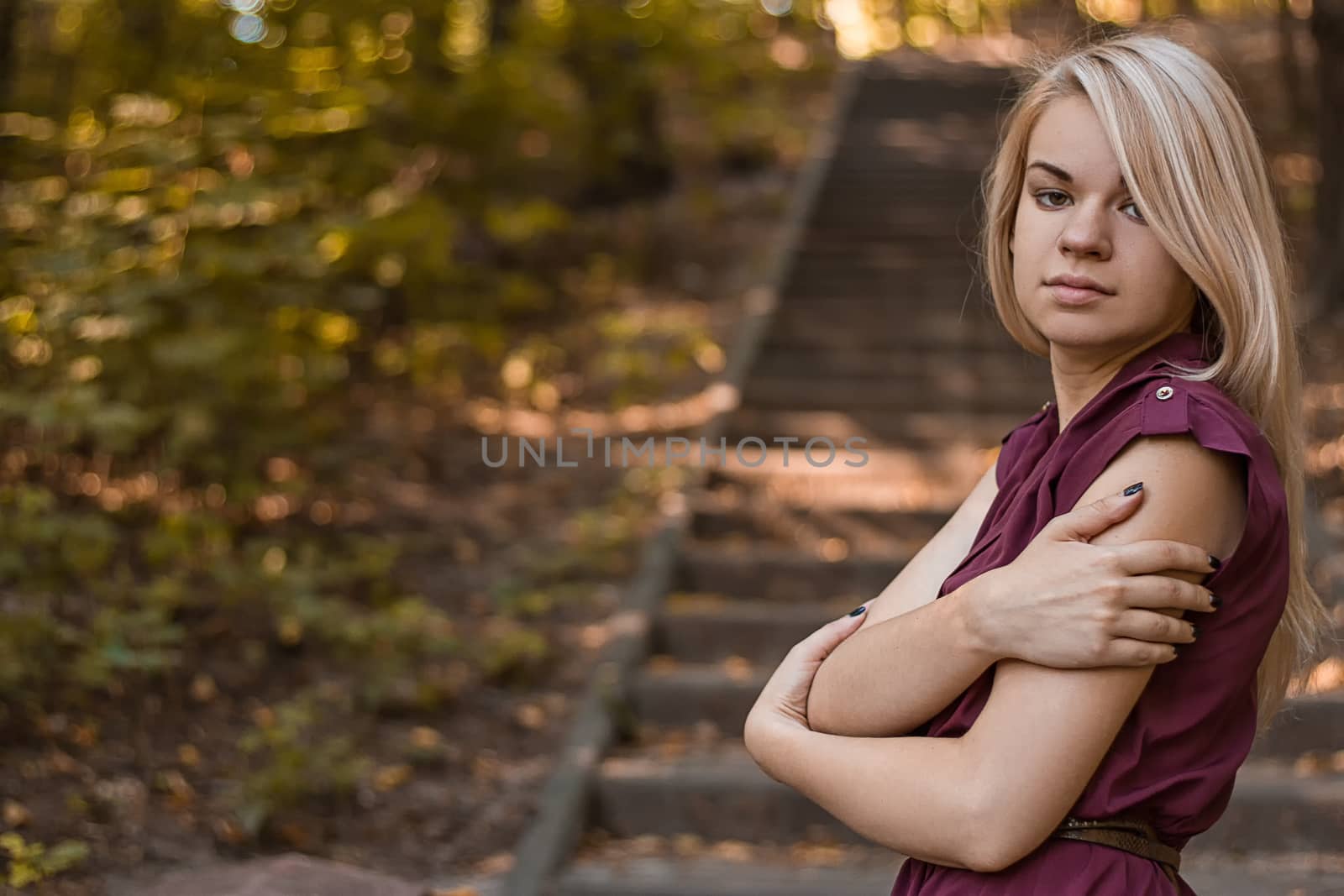 Portrait of young pretty white girl with blonde hair and in Burgundy clothes posing on the old stone staircase.