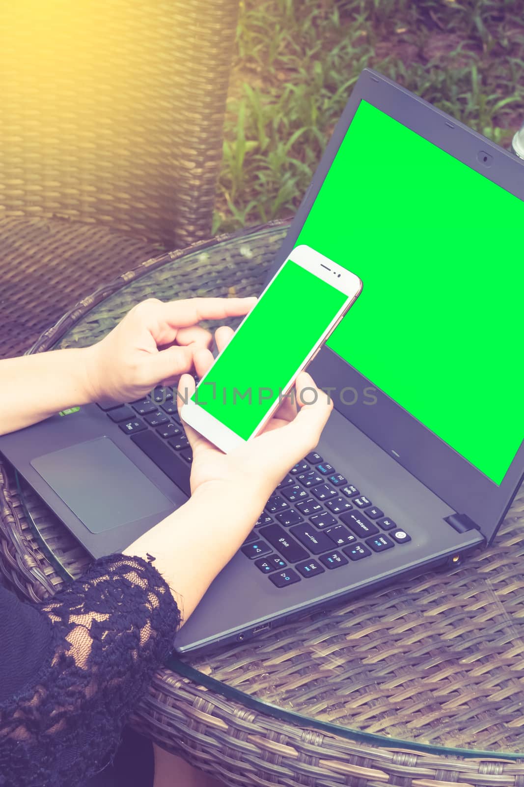 business woman working on Smartphone. There's a laptop nearby. Smartphone with green screen ready.