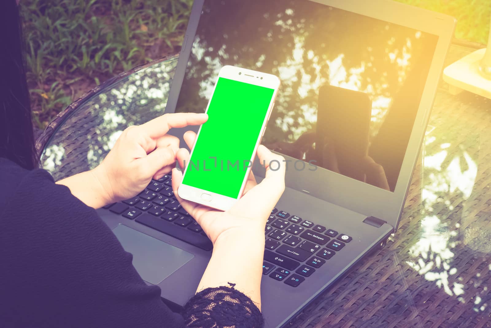 business woman working on Smartphone. There's a laptop nearby. Smartphone with green screen ready.