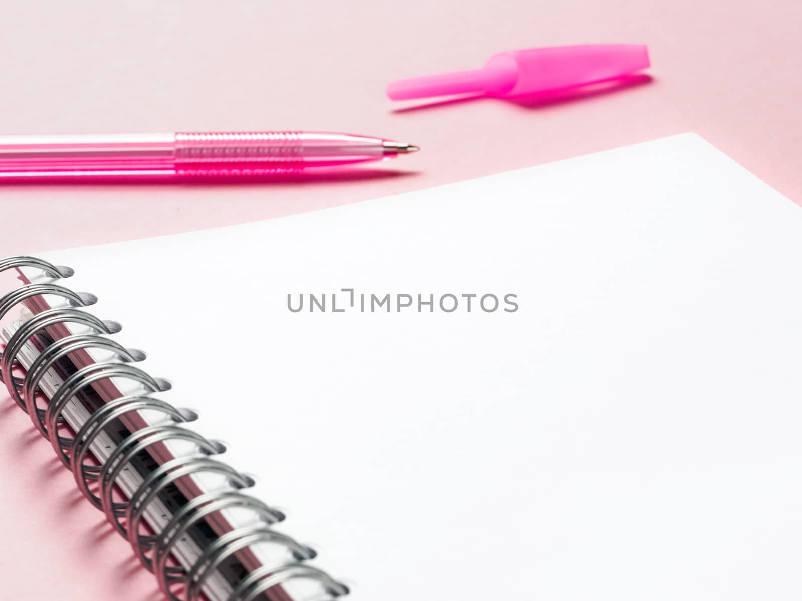 Close up view of blank note paper with pen on pink pastel background. Copy space. Back to school and education concept. Selective focus. Shallow DOF