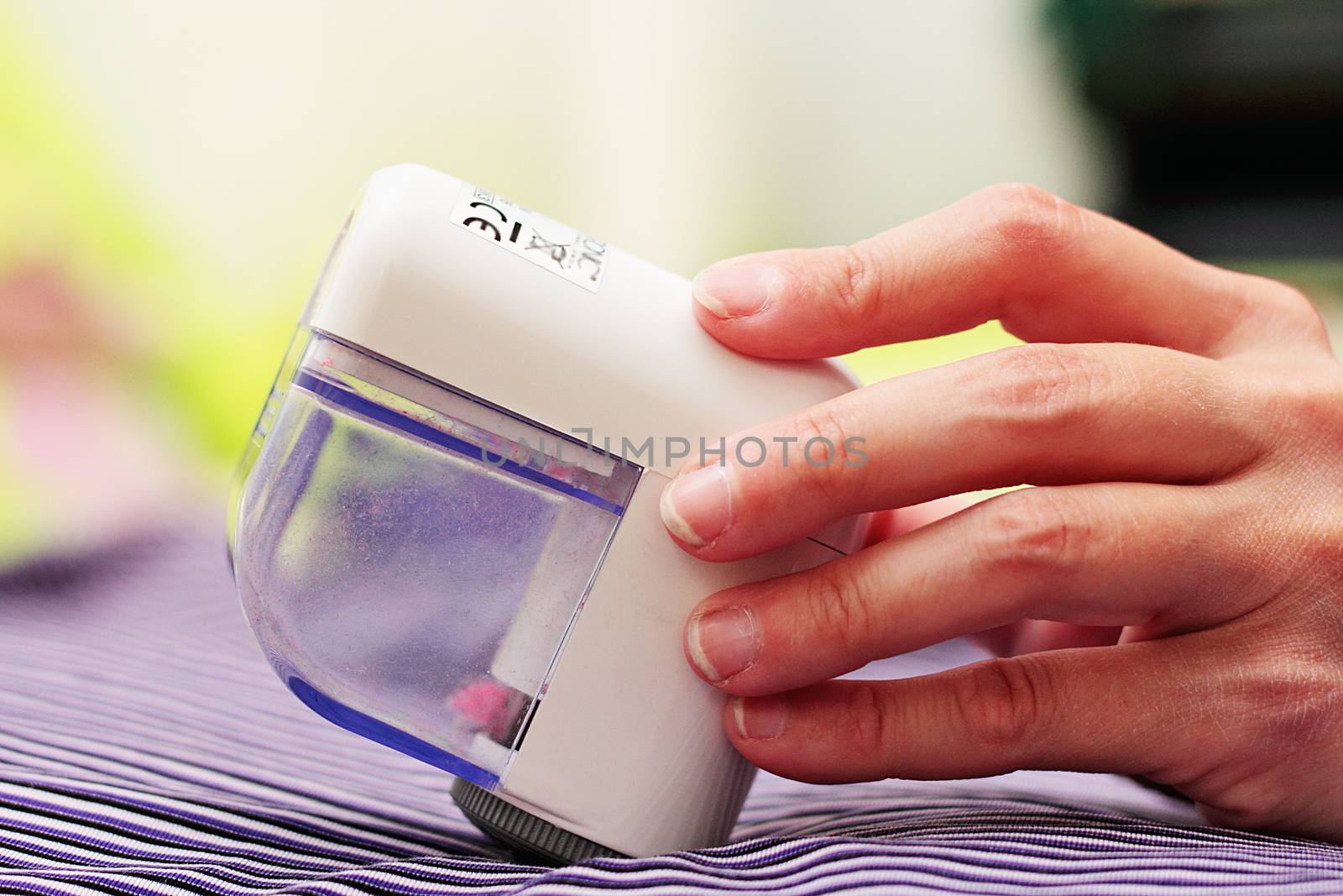 The woman removes the rolled pile from her clothes with a textile cleaning device.