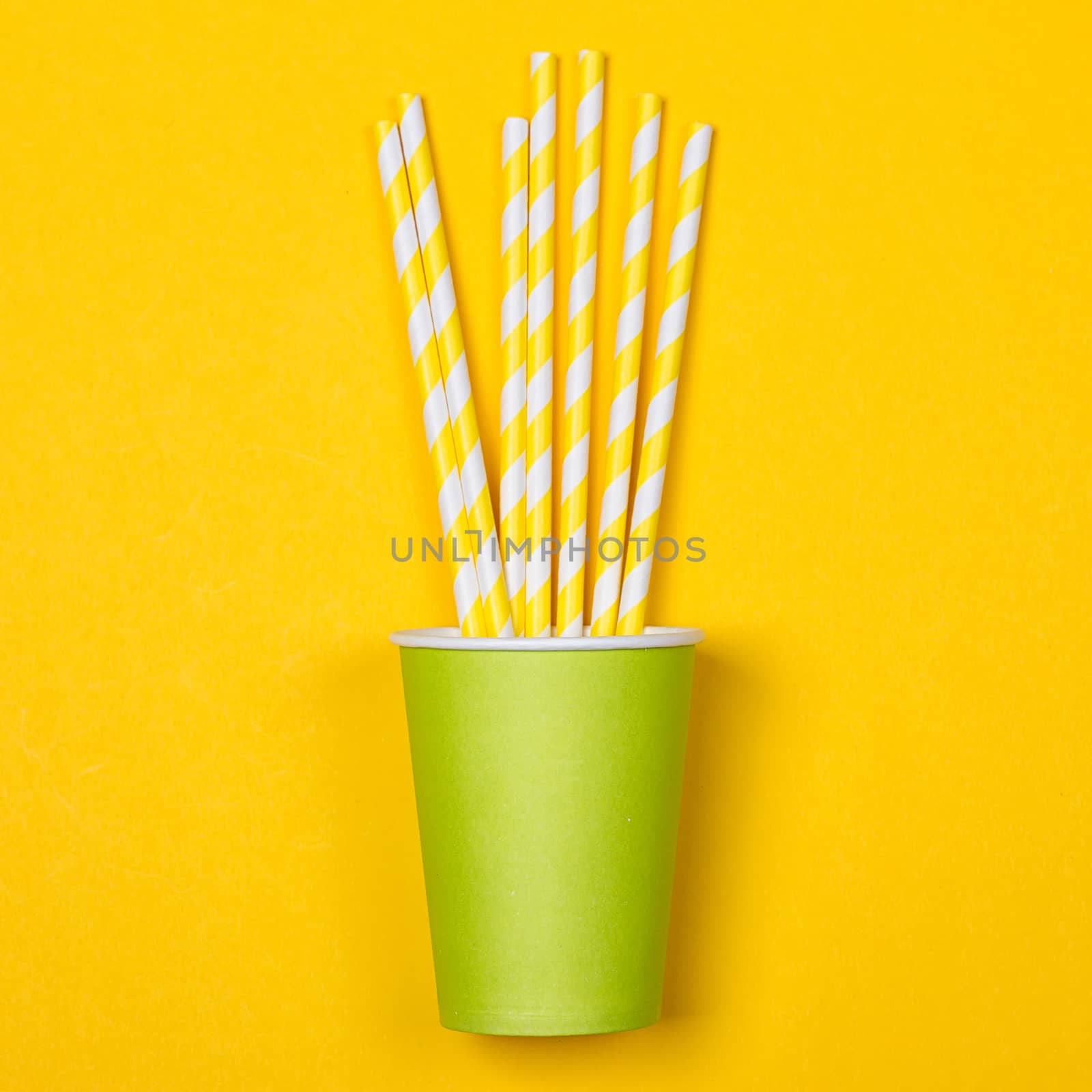 Multicolored cocktail tubes in green paper disposable cup on a yellow background