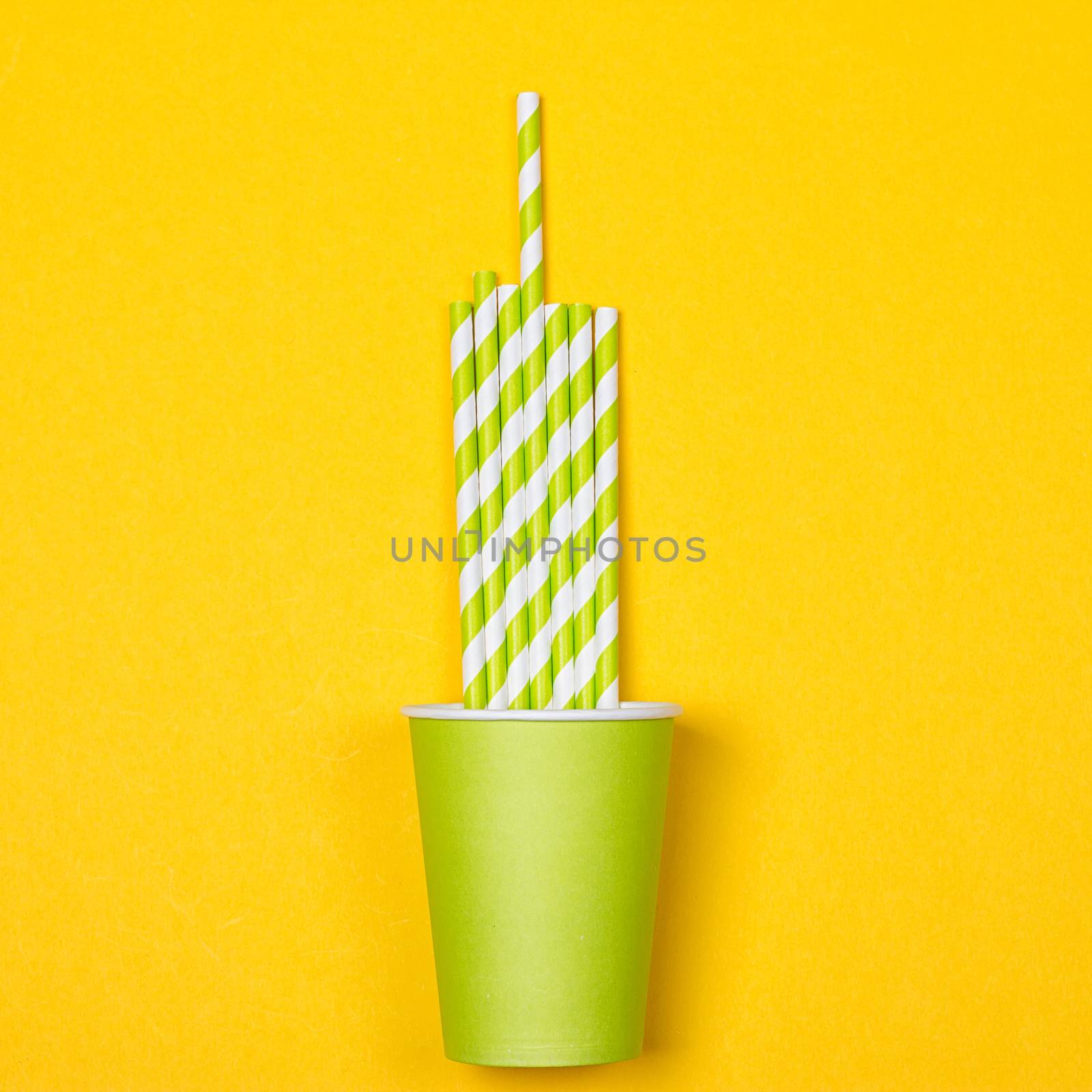 Multicolored cocktail tubes in green paper disposable cup on a yellow background