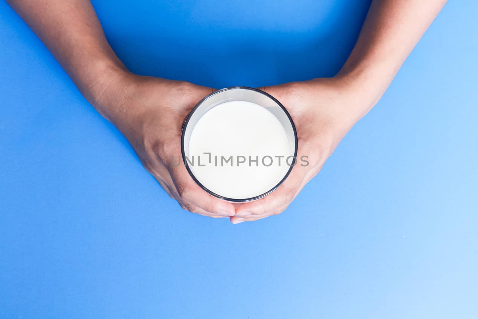 Hand holding glass of milk on blue background, food and drink fo by pt.pongsak@gmail.com