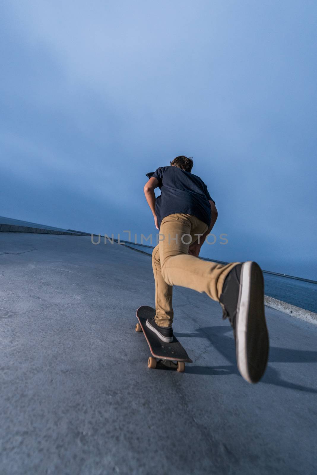 Skateboarder pushing on a concrete pavement along the harbour.