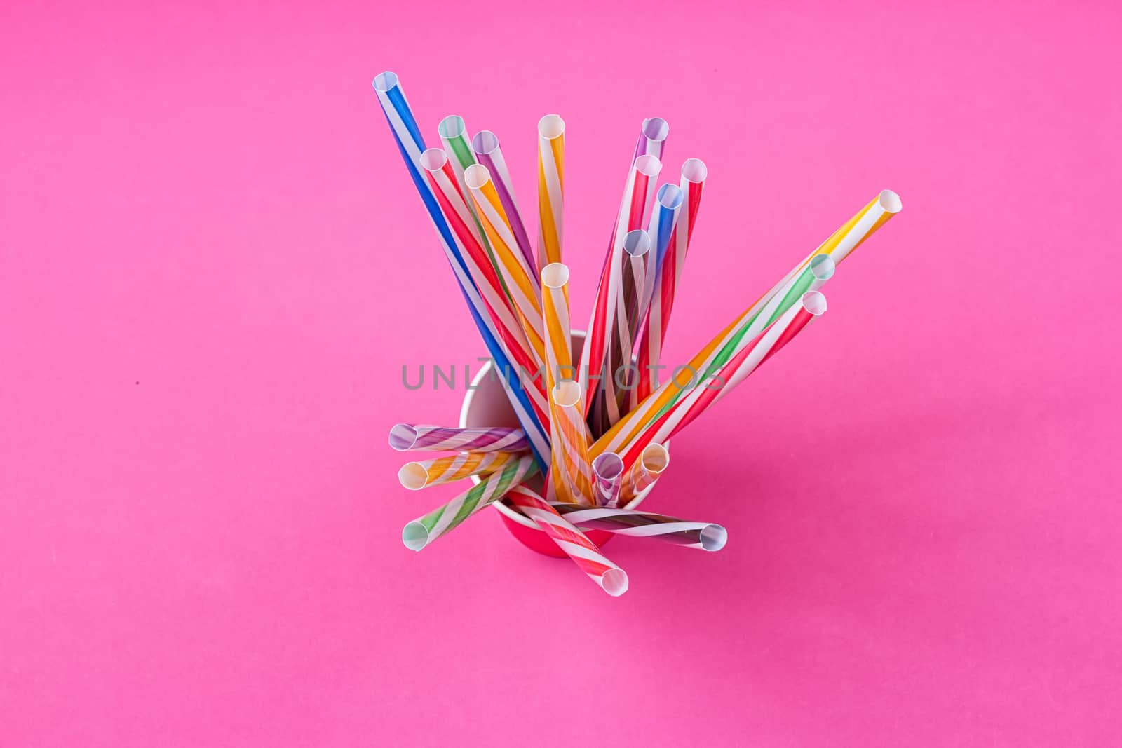 a bundle of multi-colored drinking straws in a paper Cup on a pink background. fashion minimal. flat lay