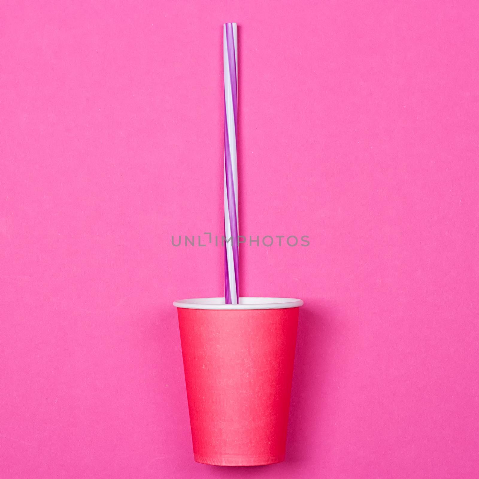 a bundle of multi-colored drinking straws in a paper Cup on a pink background. fashion minimal. flat lay