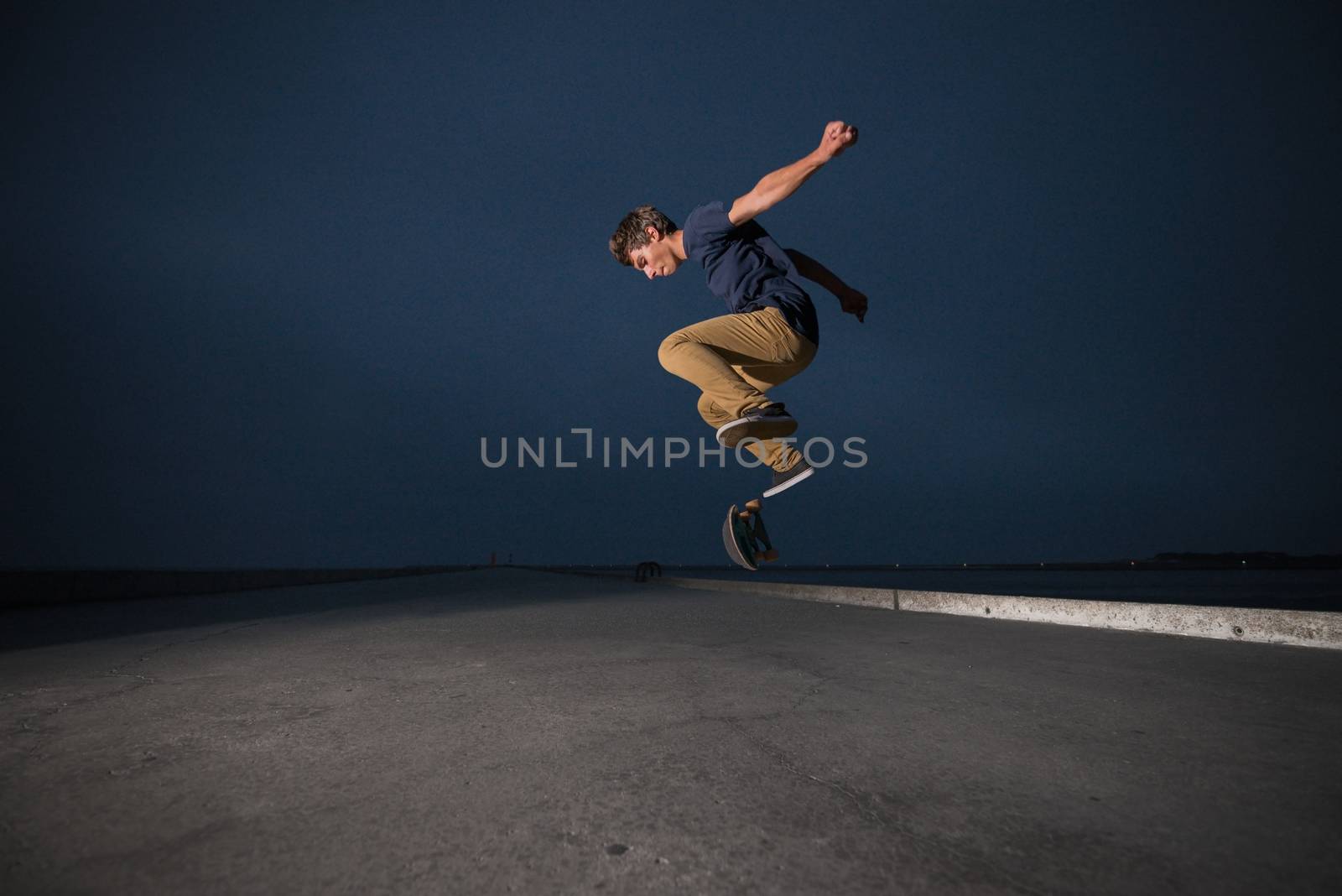 Skateboarder performing a ollie flip on a concrete pavement along the harbour.