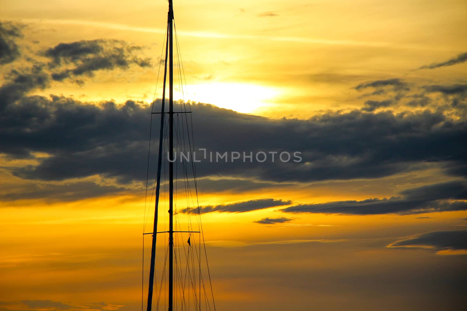 Beautiful orange sunset, a chemtrail, a few dark clouds and a boat mast in the sky in spring.