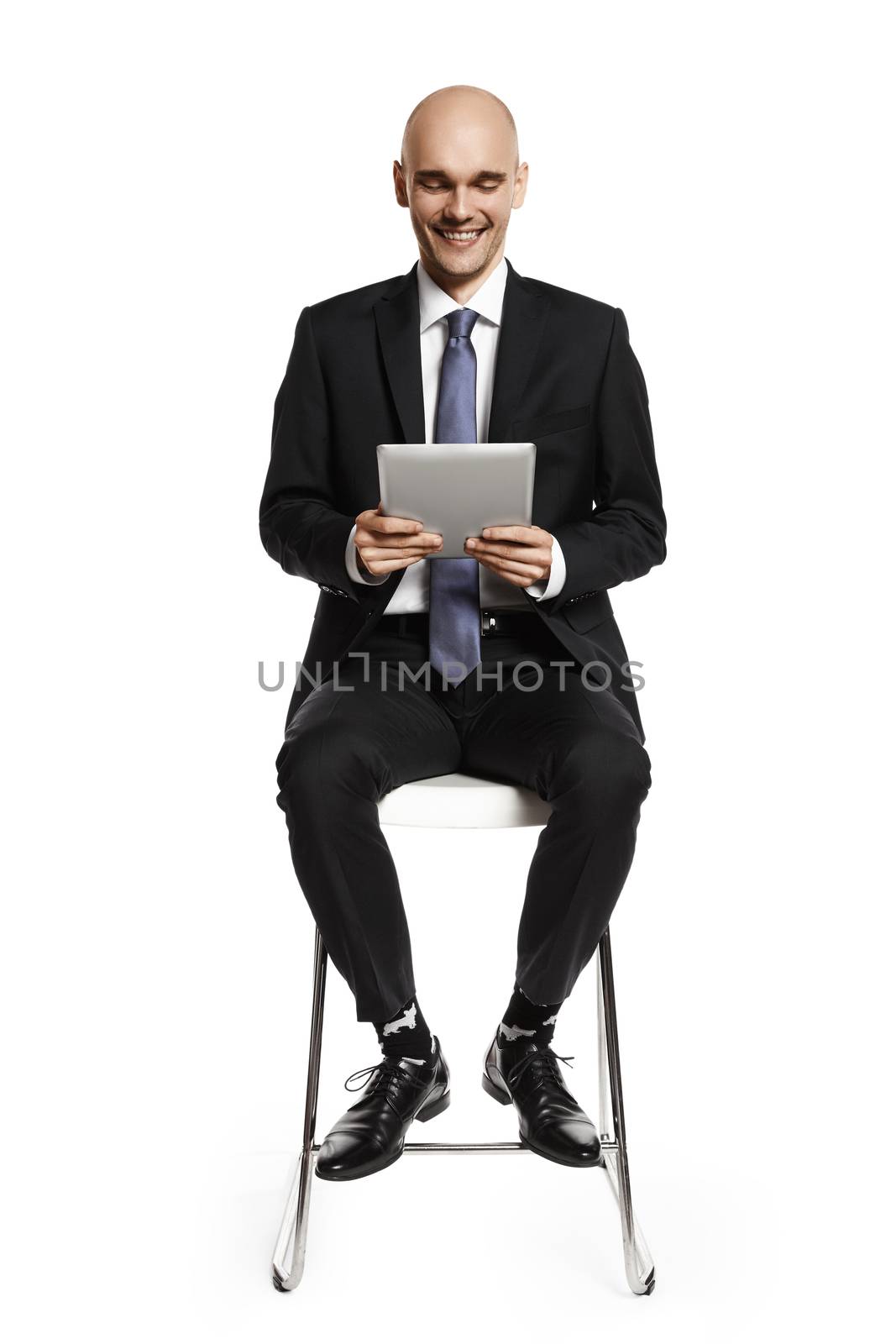 Cheerful young businessman sitting on a chair and looking at digital tablet. Isolated on white background.