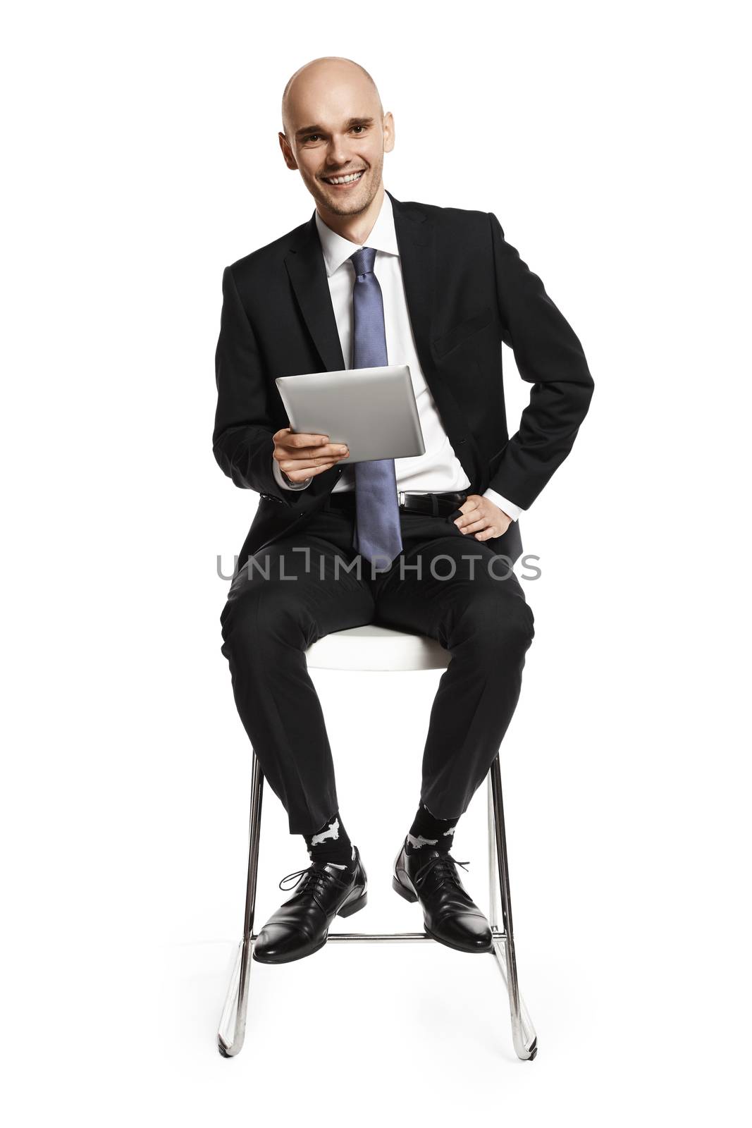 Cheerful young businessman sitting on a chair with a digital tablet. Isolated on white background.