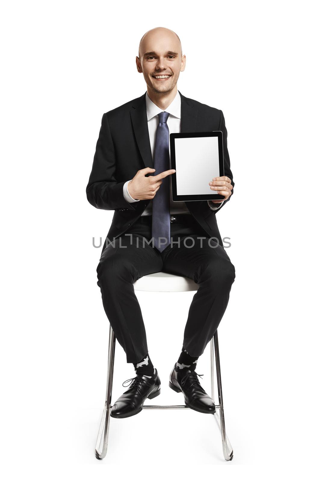Cheerful young businessman sitting on a chair and showing something on digital tablet. Isolated on white background.