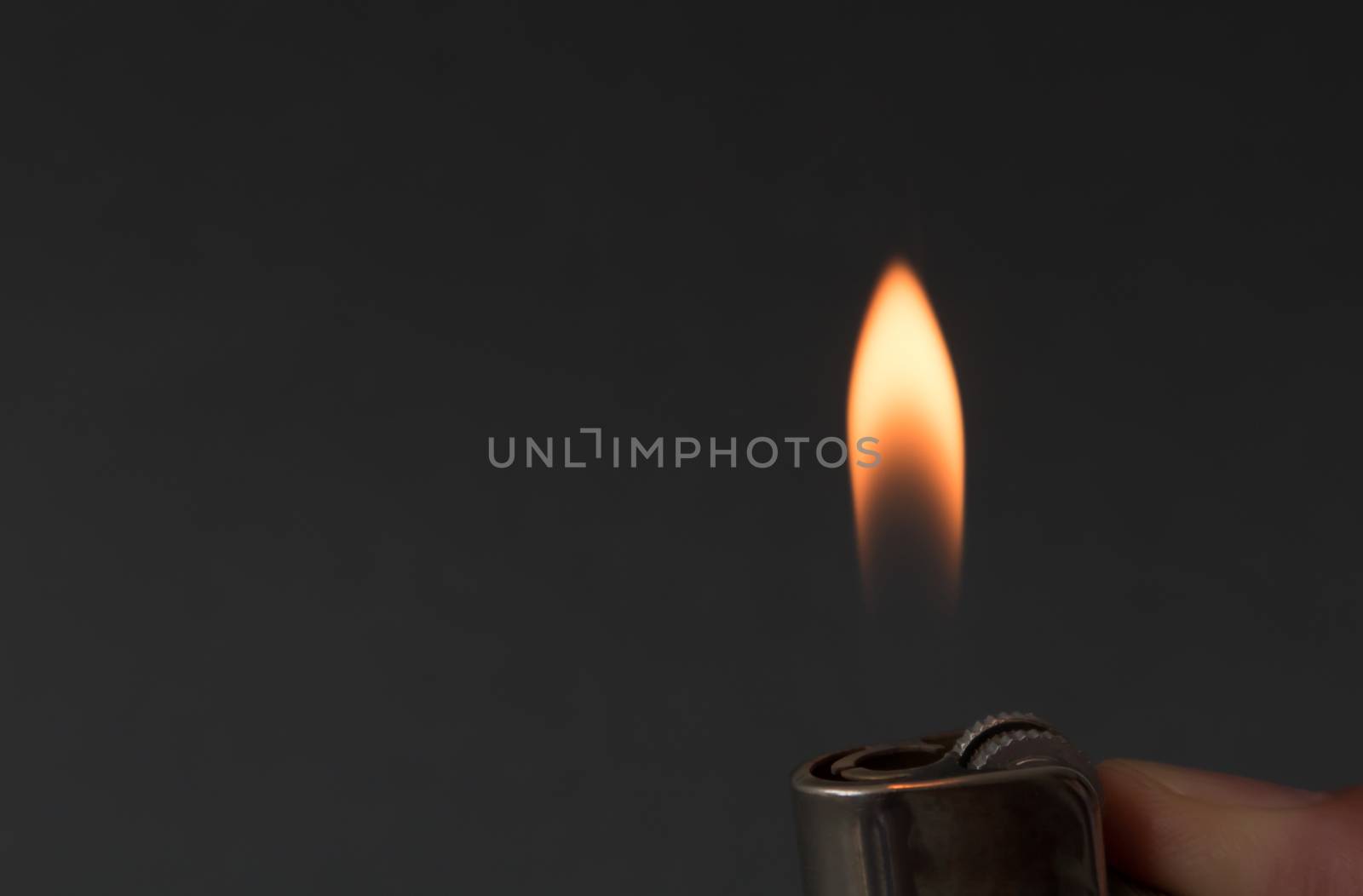 Hand igniting fire with lighter on dark background