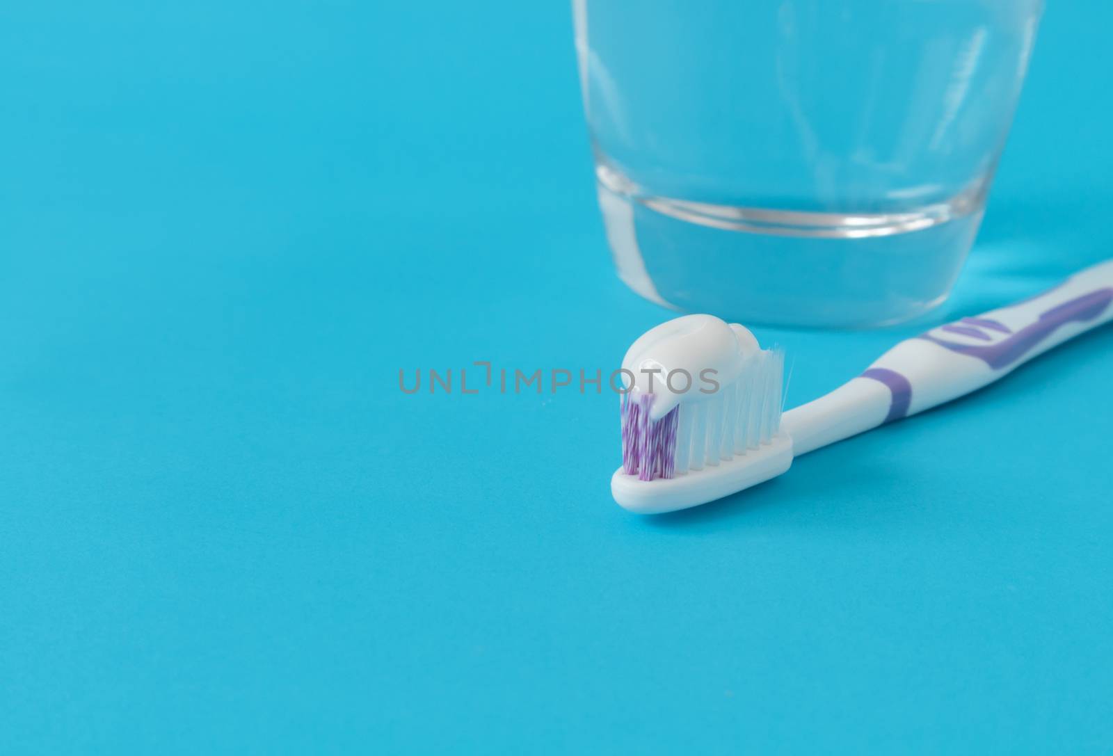 Closeup toothpaste on toothbrush with water glass on blue background