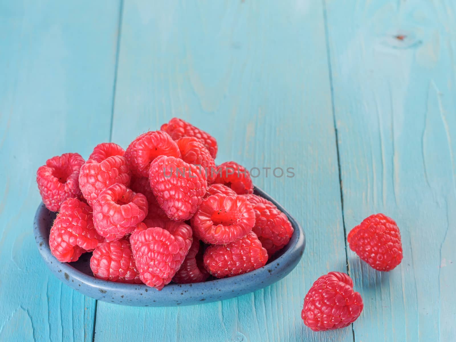Fresh raspberries on blue wooden background. Raspberry in blue trandy plate. Summer and healthy food concept. Copy space.