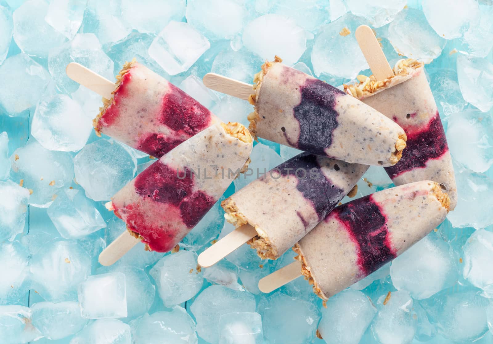 Homemade ice cream popsicle with berries, granola and chia seeds. Healthy summer breakfast concept. Popsicles from yogurt and banana with berries and granola. Top view. Copyspace