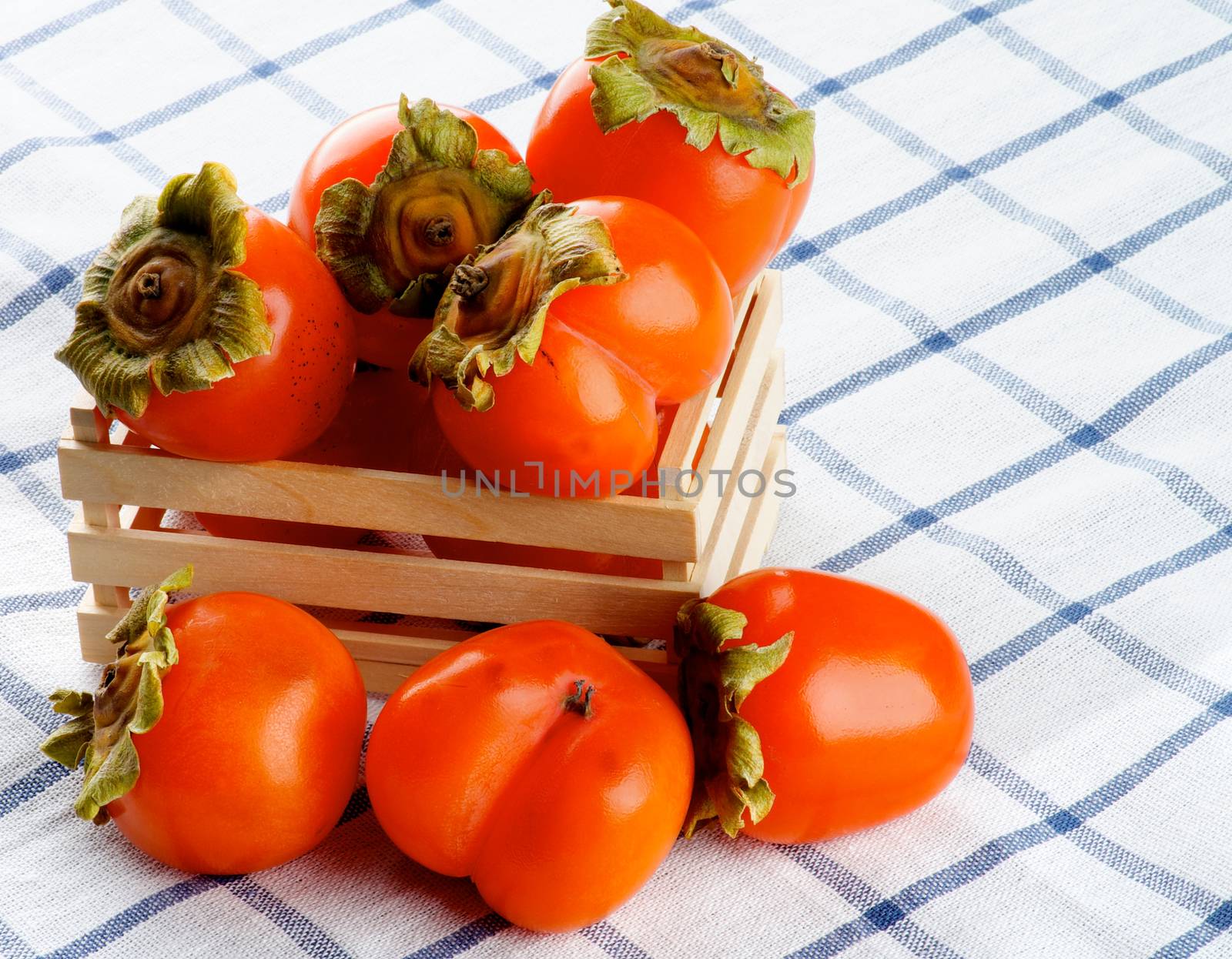 Arrangement of Delicious Raw Persimmon in Wooden Box closeup on Checkered Textile Napkin