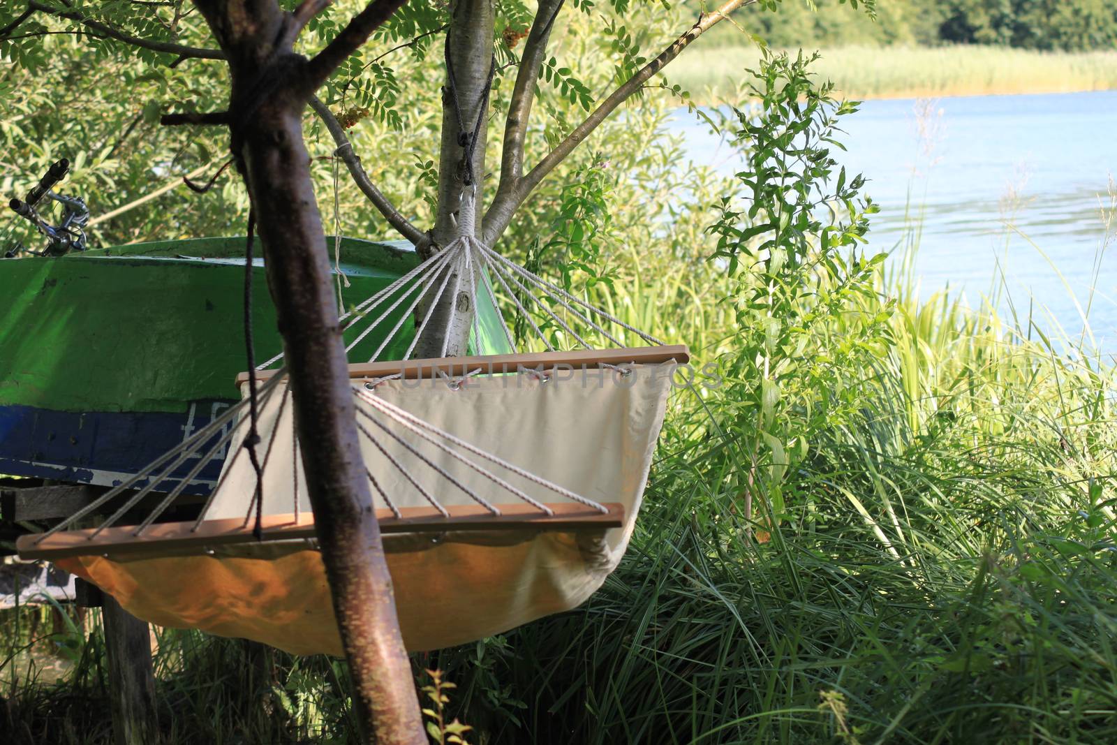 Empty hammock, boat and fishing rod among the greenery on the background of lake and forest. by Kasia_Lawrynowicz