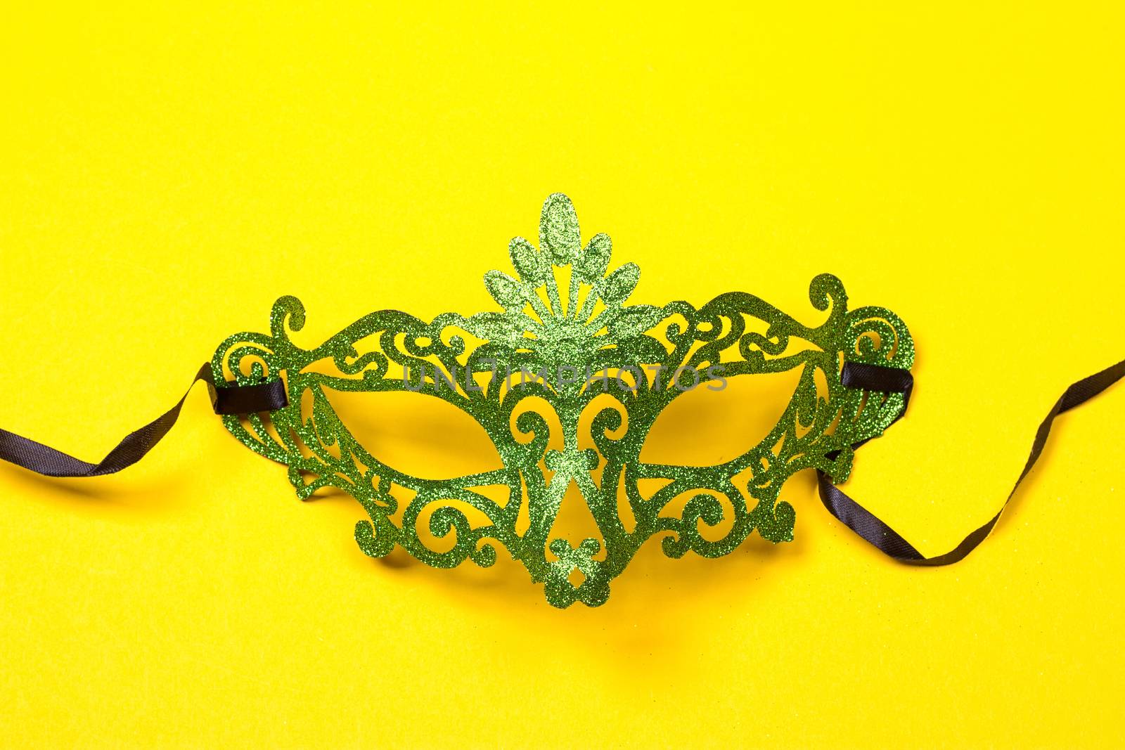 Green, mardi gras mask on a bright yellow background