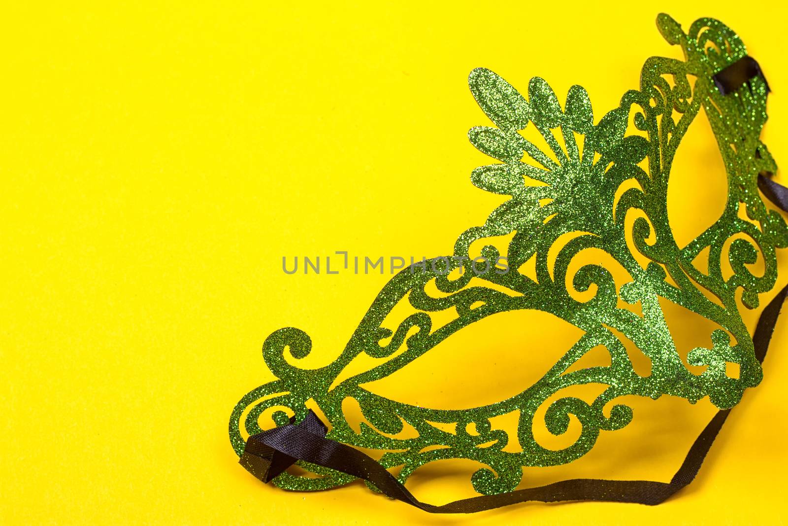 Green, mardi gras mask on a bright yellow background