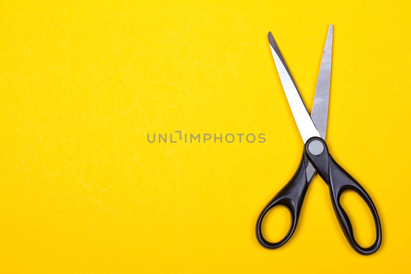 Black stationery scissors on a yellow background