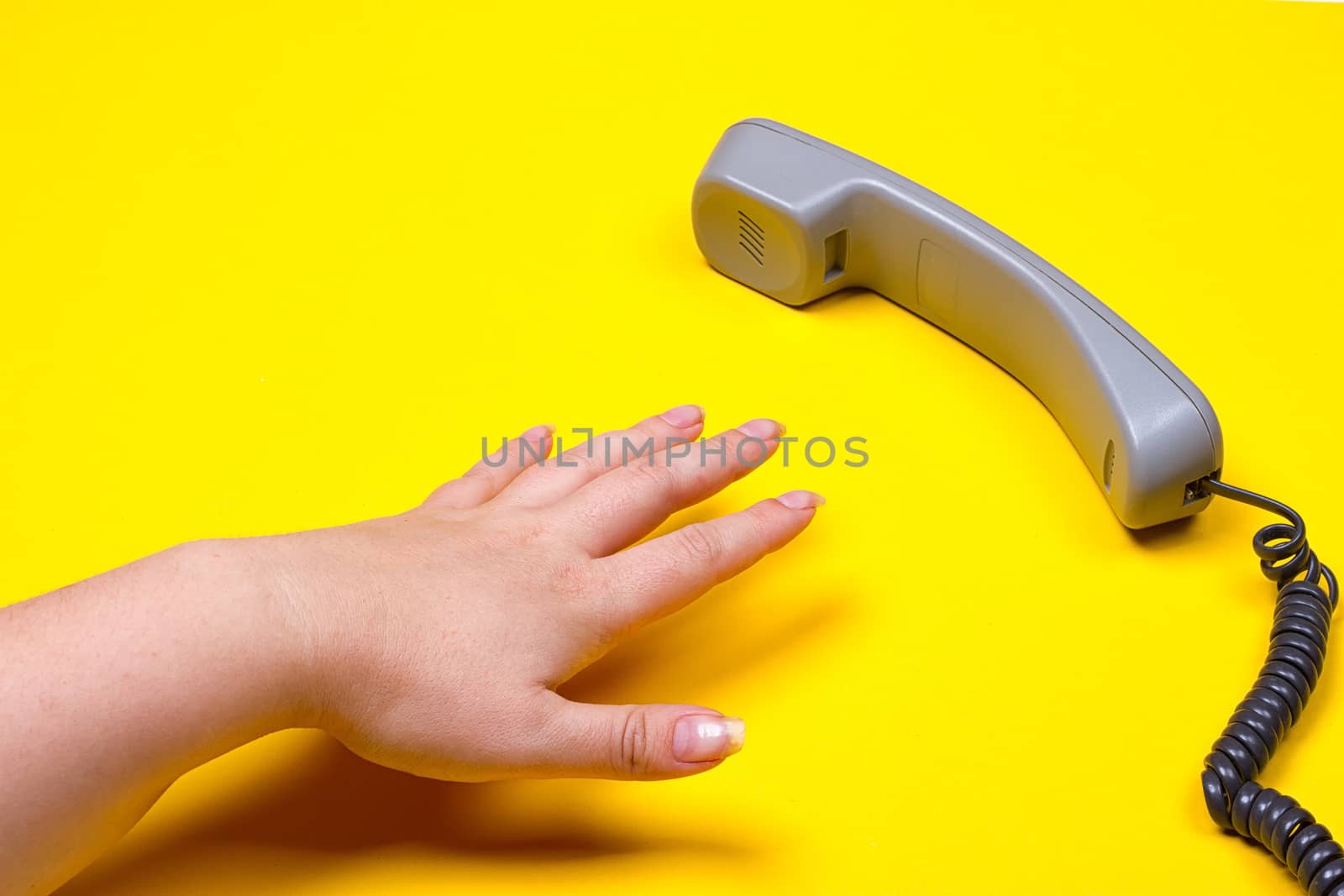 female hand lies next to the telephone receiver on the wire on a yellow background