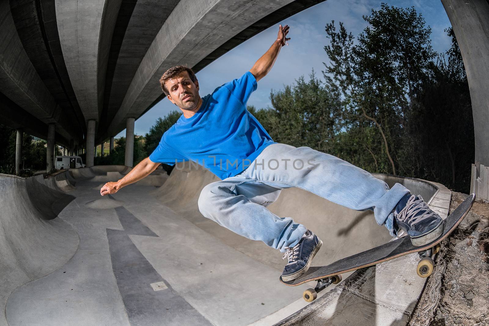 Skateboarder in a concrete skatepark under a highway bridge.