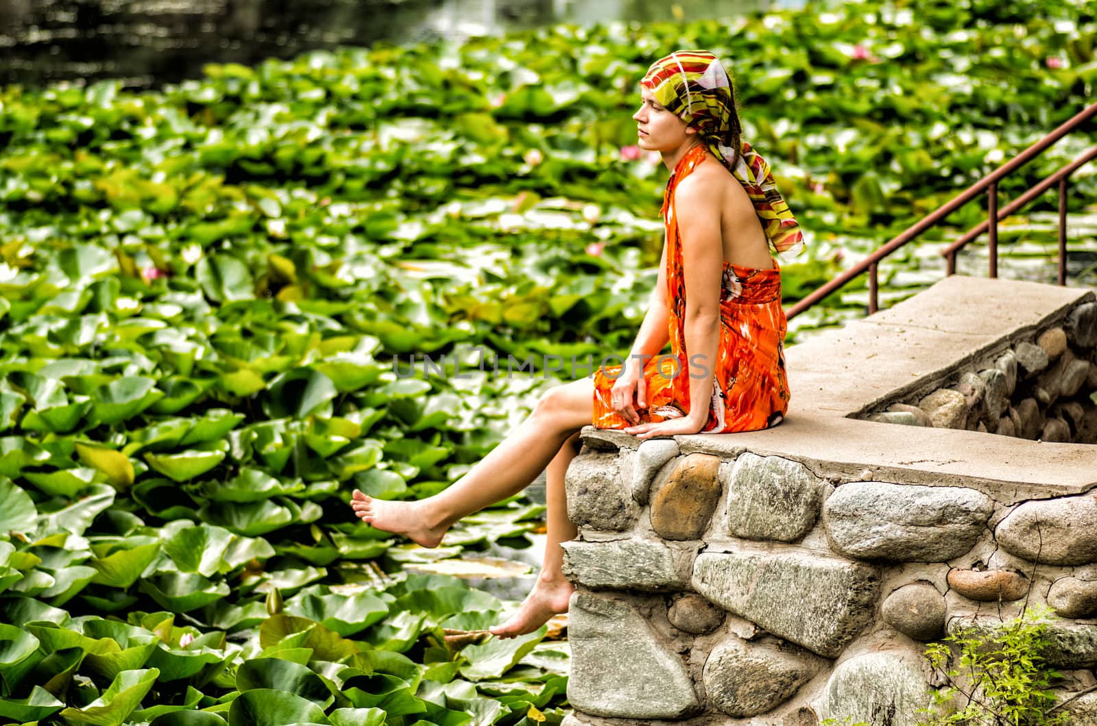 a woman is sitting on a stone pier looking at the lake with lotus