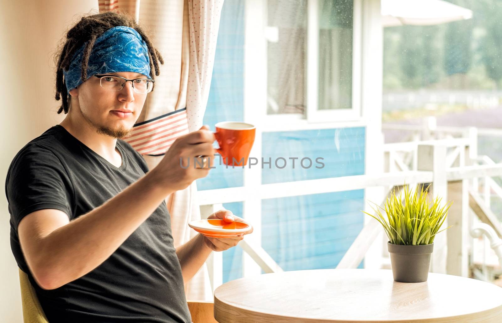 a man with dreadlocks is drinking coffee at home by Desperada